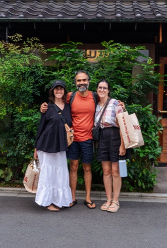 Three friends with shopping bags smiling in front of a shop hedge