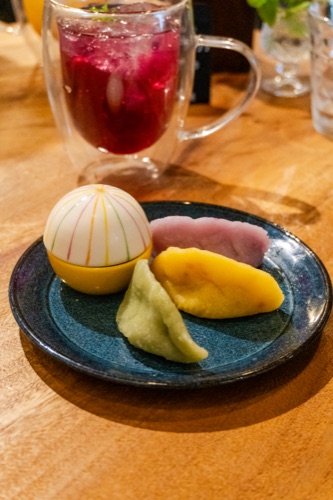 Three pieces of wagashi on a dark plate beside a glass of berry tea