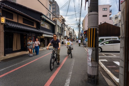 Cyclists and pedestrians on a narrow Kyoto street of timber townhouses