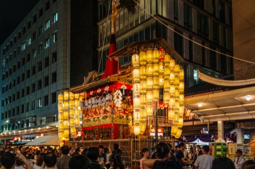 A Gion Matsuri float lit by rows of paper lanterns at night, crowds filling the street