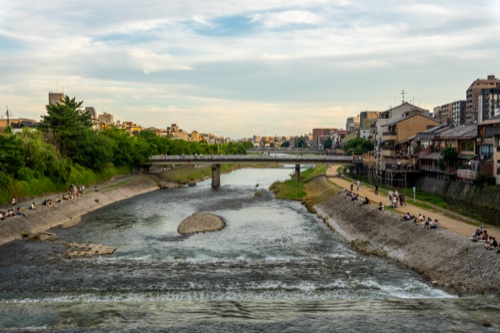 The Kamo river over a weir at dusk with people on the banks and a bridge beyond