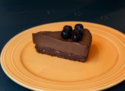A slice of chocolate tart with blueberries on a mustard yellow plate