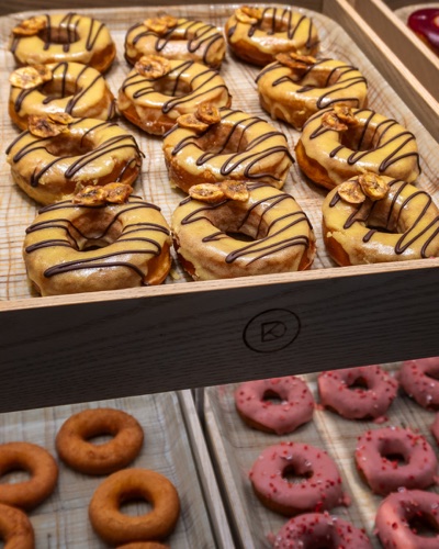 Trays of glazed and chocolate drizzled doughnuts in a bakery case