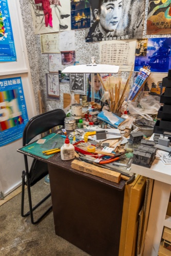 A cluttered artist's desk under pinned sketches, posters and brushes