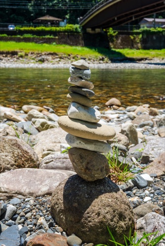 A stacked river stone cairn on a gravel bank below a road bridge