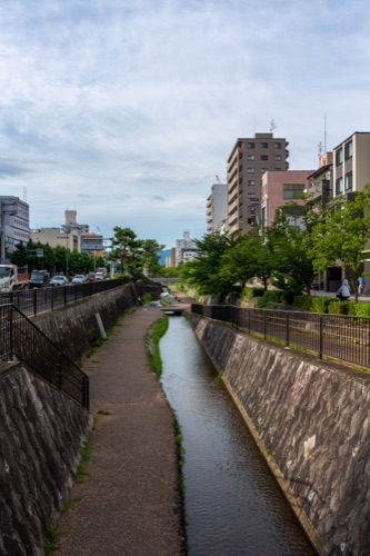 A narrow stone lined canal running between apartment blocks and trees