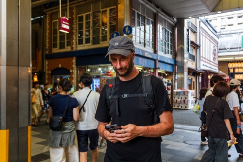 A man in a cap and black tee checking his phone in a covered shopping arcade