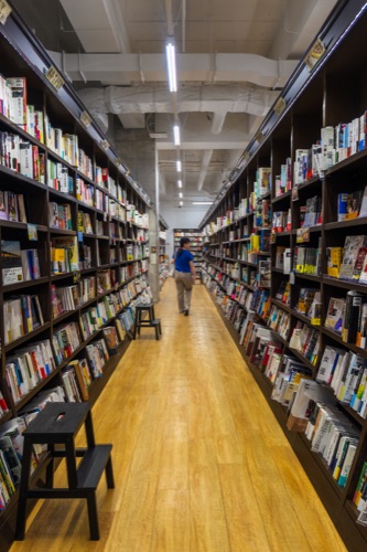 A long aisle of a Japanese bookshop with a reader at the far end