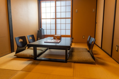 A tatami room with low table and legless chairs lit through shoji screens