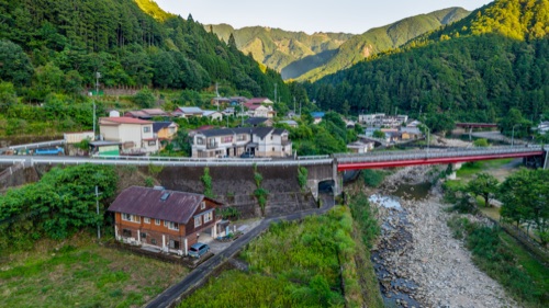 A red road bridge over a boulder strewn river in a mountain village, seen from above