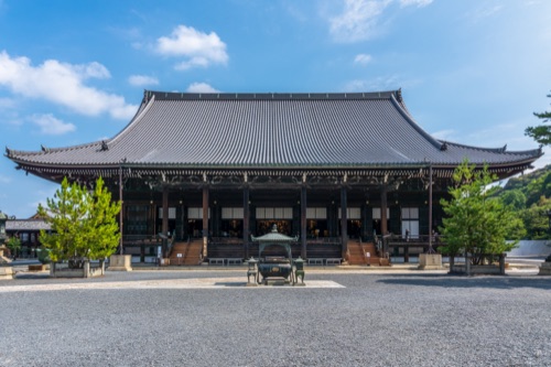 The broad tiled hall of a Kyoto temple across an empty gravel forecourt under blue sky