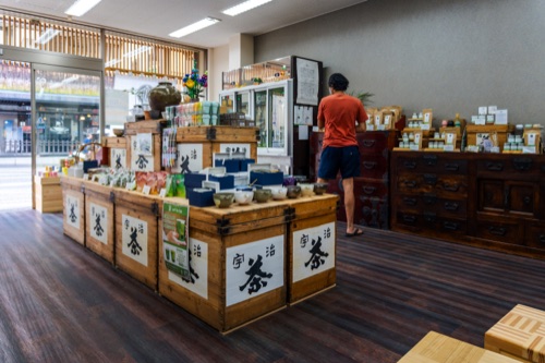 A tea shop interior with timber crates of tea tins and a staff member at the counter
