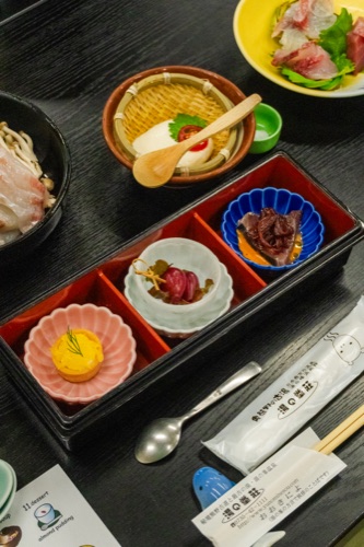 A lacquered bento tray with small dishes of pickles, fish and a chestnut sweet