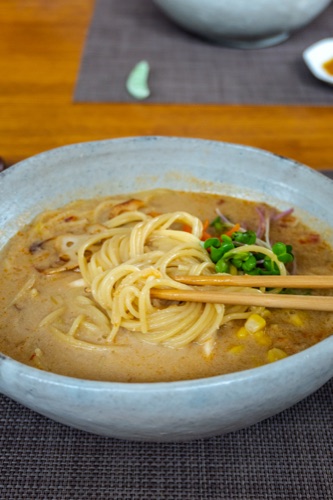 A bowl of udon in a creamy miso broth with corn and spring onion