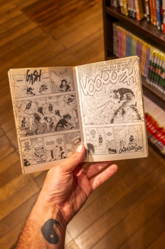 A hand holding open a small manga volume in a manga library