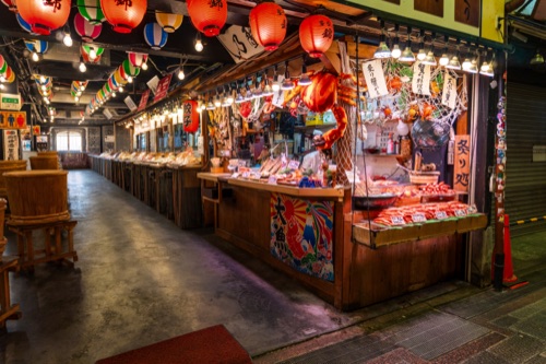 A covered market street at dusk strung with red lanterns and lit stalls