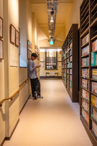 A long library corridor of manga shelves with a reader at the end