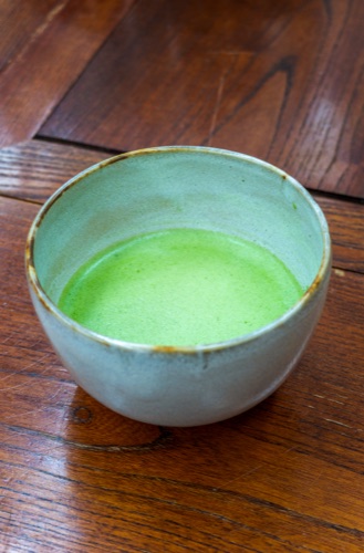 A bowl of bright green matcha on a dark timber table