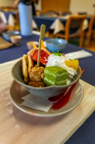 A matcha parfait with sponge, fruit and cream in a stoneware bowl