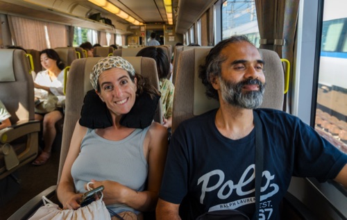 Two travellers settled into a train carriage, one in a headscarf, one in a dark tee