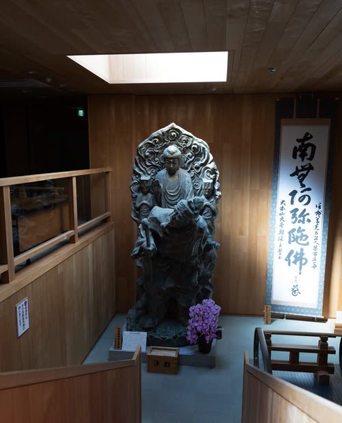 A dark bronze seated Buddha in a wood-panelled temple hall beside a calligraphy banner