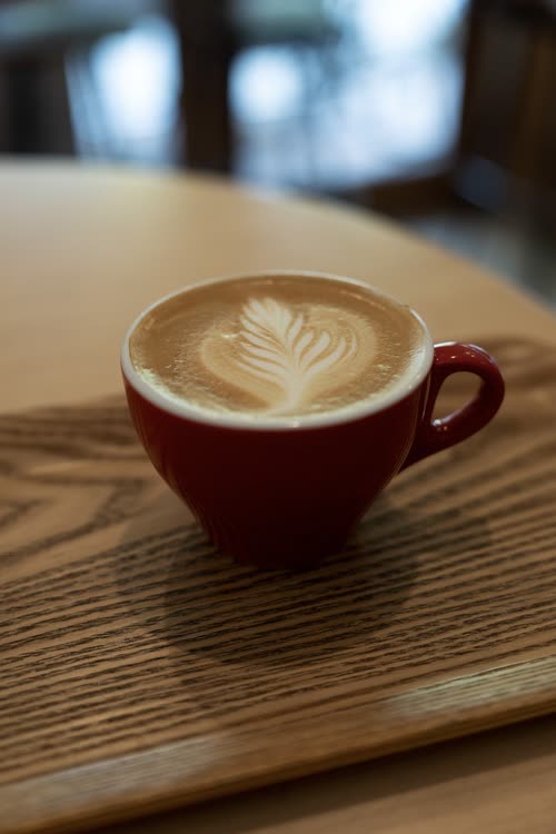 A latte with rosetta art in a red cup on a wooden table