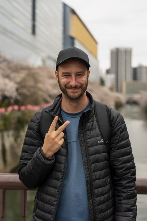 Jordy Scott raising a peace sign on a blossom-lined canal bridge in Tokyo