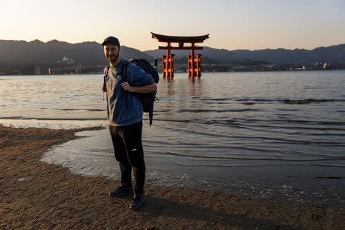 Jordy Scott on the sand at Miyajima with the floating torii gate behind him