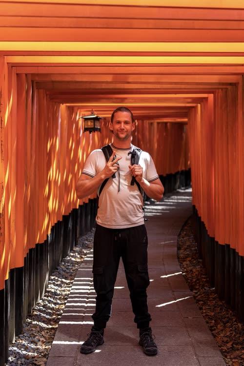 Jordy Scott standing in the vermilion torii tunnel at Fushimi Inari, Kyoto