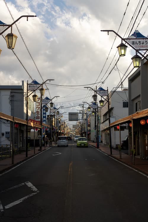 A quiet regional Japanese high street under lamp posts and overhead wires