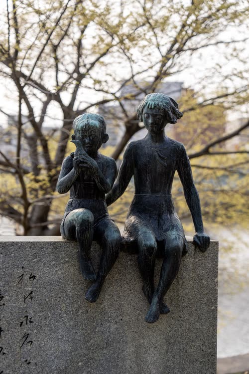 A bronze memorial sculpture of two children seated on a stone plinth, Hiroshima