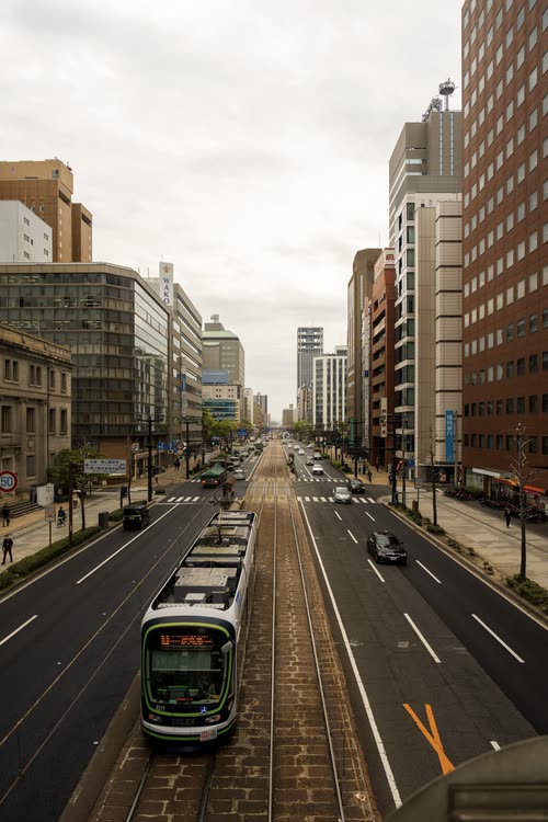 A green tram running down a wide Hiroshima street between office buildings