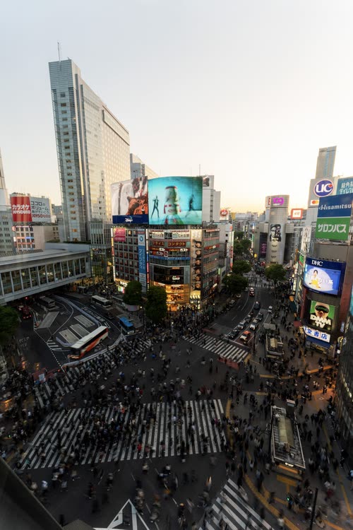 Shibuya Crossing seen from above as crowds flood the intersection at dusk