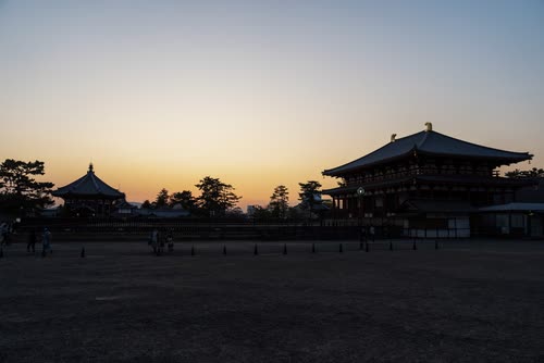 Temple halls silhouetted against a dawn sky over an open gravel courtyard