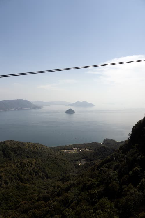 A ropeway cable crossing above forested slopes and the calm inland sea