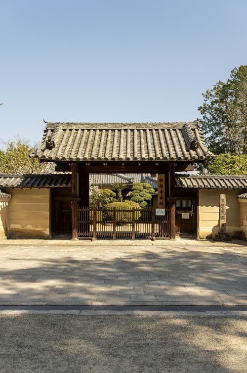 A tiled temple gate and white plaster wall under a clear blue sky