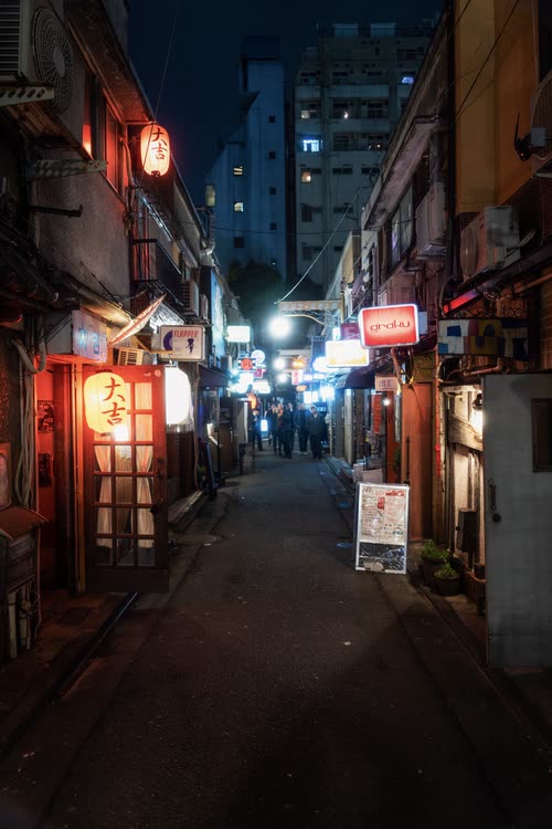 A narrow alley of small bars lit by red lanterns at dusk
