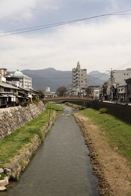 A concrete-lined river running through a Japanese town toward distant mountains