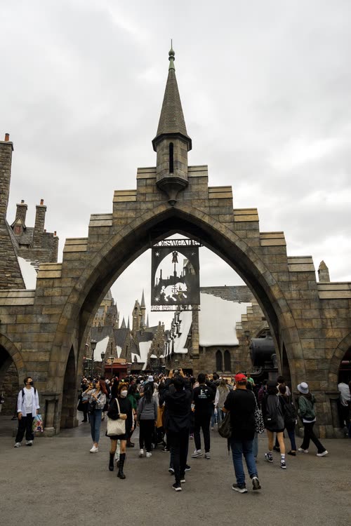 Visitors passing through the stone archway into a themed castle area of the park