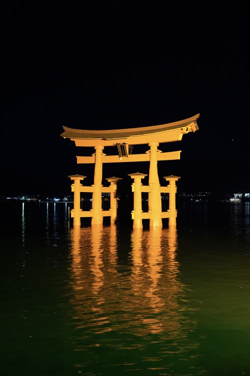 The Itsukushima torii gate floodlit gold above its reflection at night