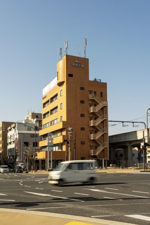 A van passing a tan apartment block beside an elevated rail line