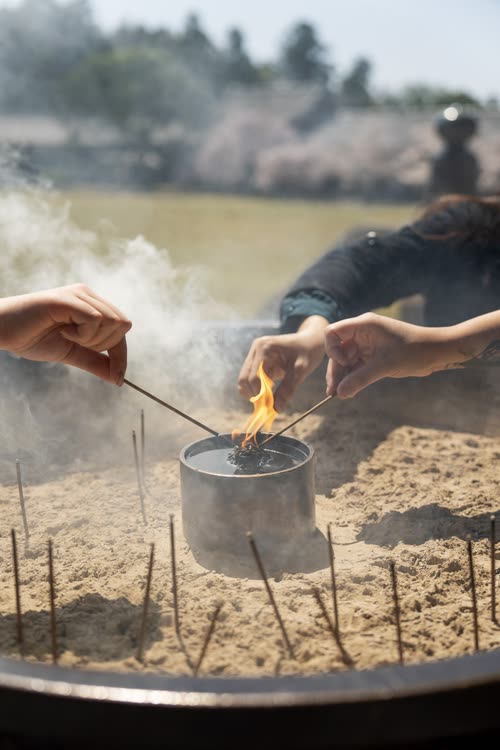 Hands lighting incense sticks at a temple burner in Nara