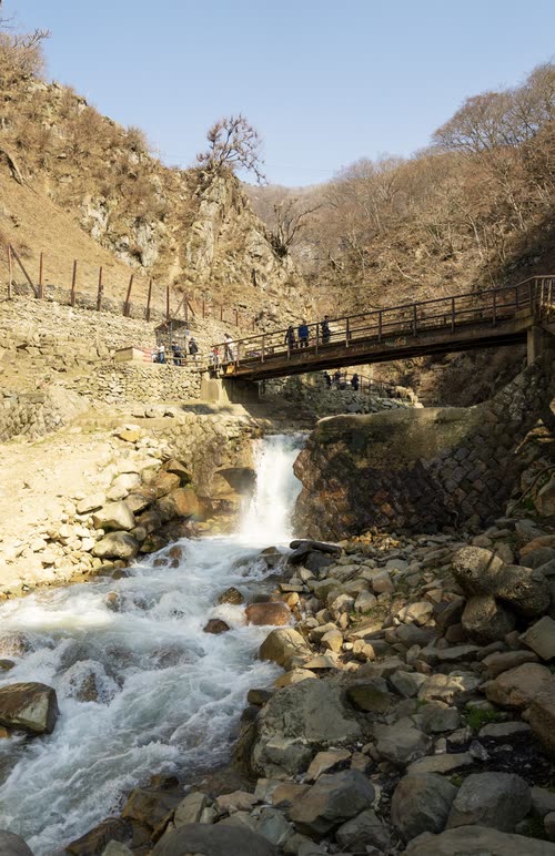 Meltwater rushing over boulders beneath a wooden footbridge in a steep Japanese gorge