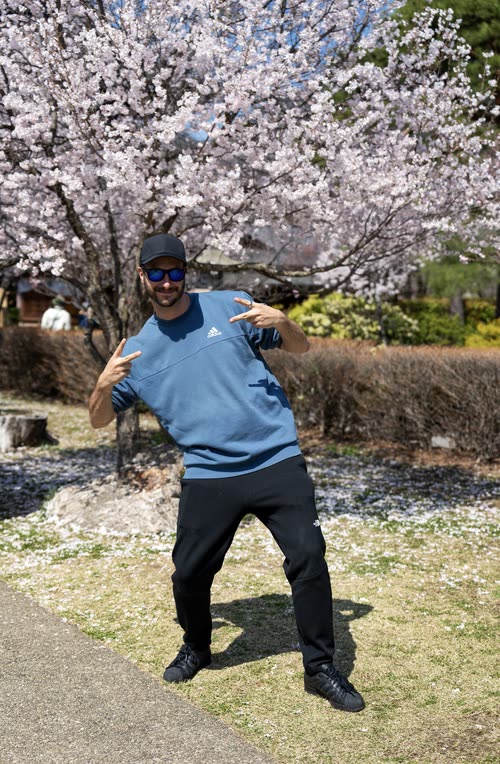 Jordy Scott posing beneath a cherry tree in full bloom on a bright spring day