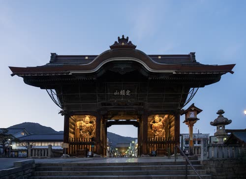 A temple gate lit from within at dusk, guardian statues flanking the entrance
