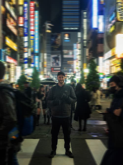 Jordy Scott standing on a neon-lit Shinjuku street at night as crowds blur past