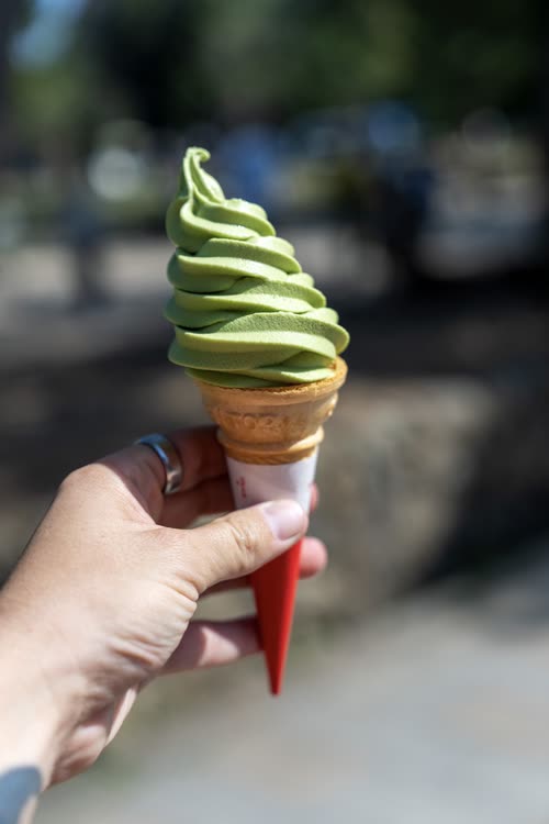 A matcha soft serve cone held up against a blurred Kyoto street