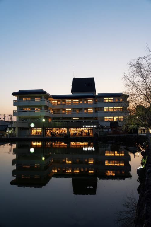 A lit riverside building mirrored in still water at blue hour