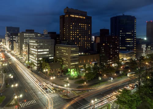 A long exposure of a city intersection and office towers in Hiroshima at night