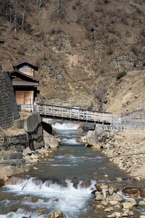 A hot spring stream running under a wooden footbridge in a Nagano valley